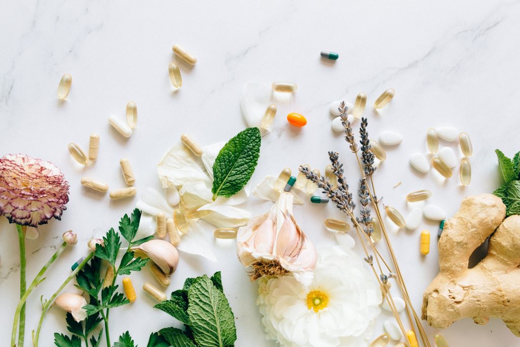 A flat lay of Alternative medicines like ginger, spearmint, flowers, gel capsules